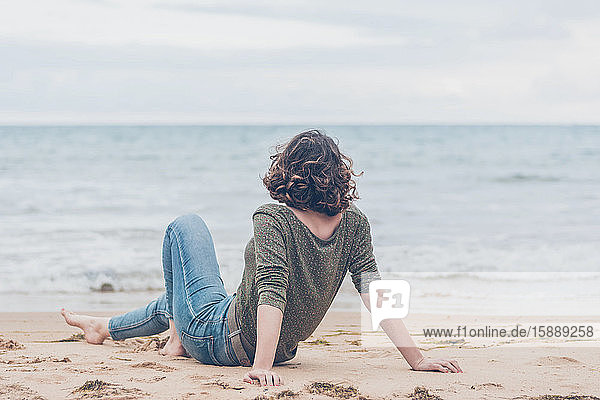 Junge Frau sitzt am Strand und schaut auf das Meer