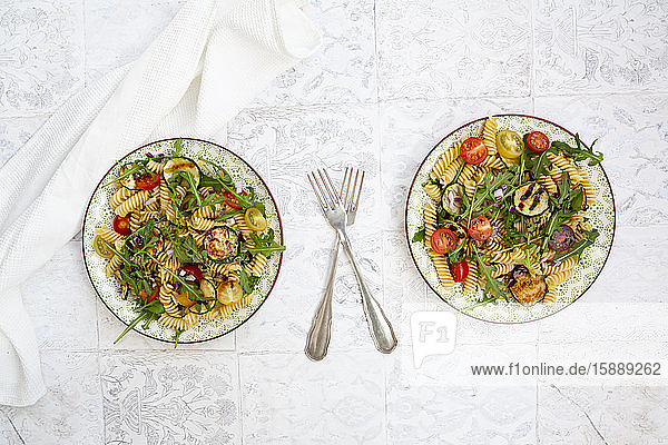 Zwei Teller vegetarischer Nudelsalat mit gegrillten Zucchini  Tomaten  Rucola  roten Zwiebeln und Balsamico-Essig