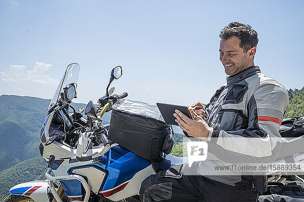Motorradfahrer auf einer Reise  der mit Tablet eine Pause in den Bergen einlegt  Pistoia  Toskana  Italien