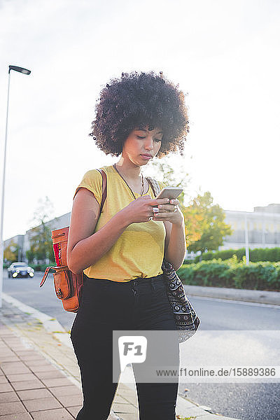 Junge Frau mit Afro-Frisur benutzt Smartphone in der Stadt