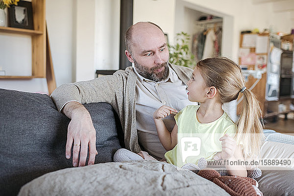 Vater und kleine Tochter sitzen zu Hause zusammen auf der Couch und amüsieren sich