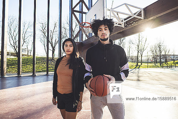 Porträt eines jungen Mannes und einer jungen Frau auf einem Basketballplatz im Gegenlicht