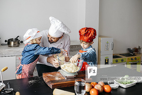 Vater mit zwei Kindern bereitet zu Hause in der Küche Teig für selbstgemachte glutenfreie Nudeln zu