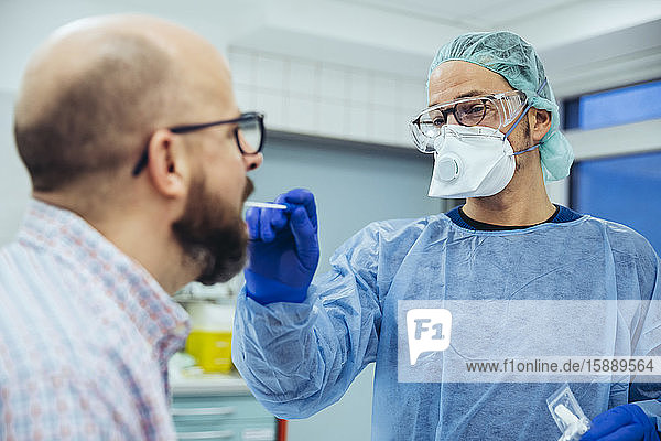 Arzt im Krankenhaus  der einen Abstrich aus dem Mund des Patienten nimmt