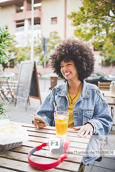 Glückliche junge Frau mit Afrofrisur in einem Straßencafé in der Stadt