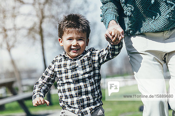 Porträt eines glücklichen kleinen Jungen  der Hand in Hand mit seiner Mutter in einem Park läuft