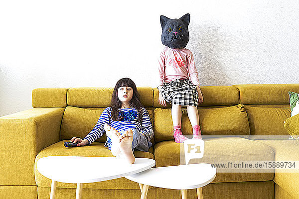 Two bored girls sitting on couch  watching TV  one wearing cat mask