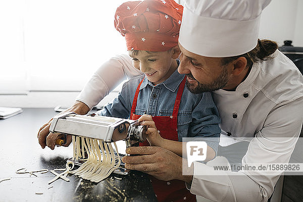 Father and son making homemade pasta with pasta machine in kitchen at home