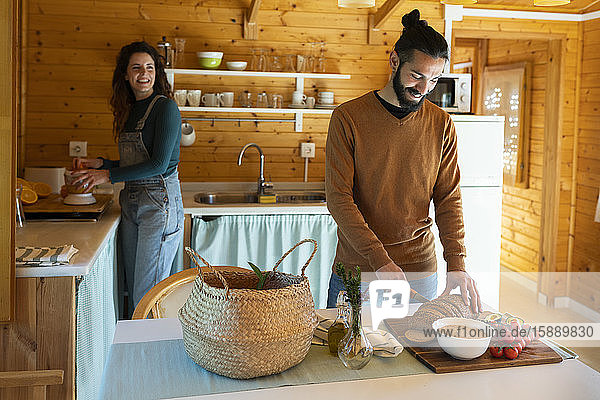 Junger Mann mit Freundin in einer Holzhütte beim Brotschneiden