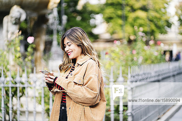 Lächelnde junge Frau benutzt Smartphone in der Stadt