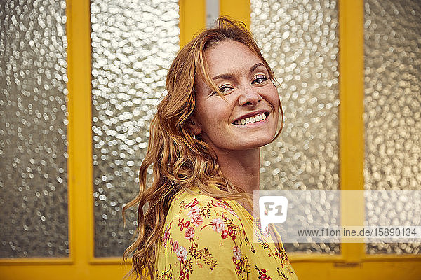 Porträt einer rothaarigen glücklichen Frau vor der Tür  die in die Kamera lächelt