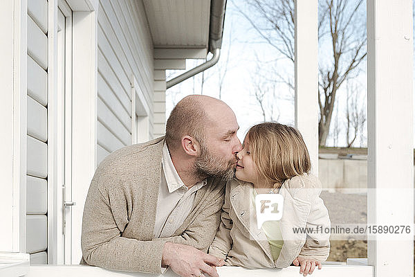 Vater küsst Tochter auf der Veranda ihres Hauses