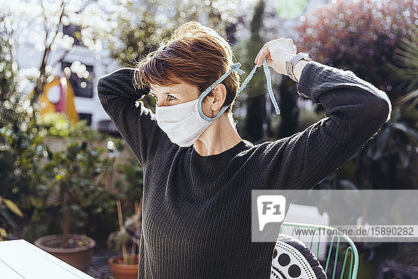 Woman siting in garden  putting on face mask
