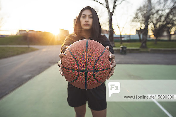 Junge sportliche Frau posiert bei Sonnenuntergang mit Basketball auf dem Platz