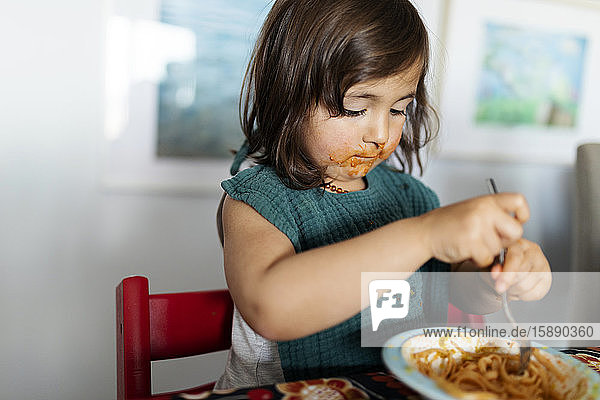 Porträt eines kleinen Mädchens mit verschmiertem Gesicht  das Nudeln isst