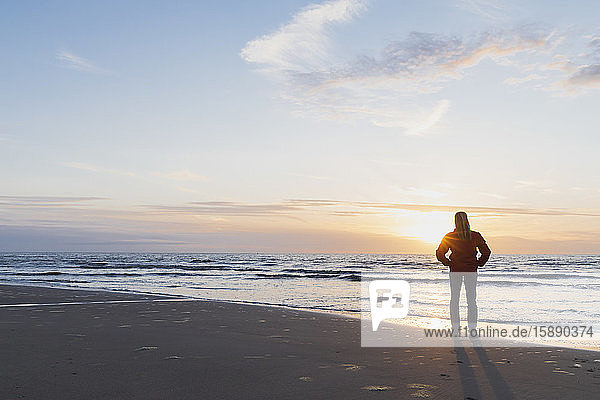 Full length of woman standing on shore while looking at sea against sky during sunset  North Sea Coast  Flanders  Belgium