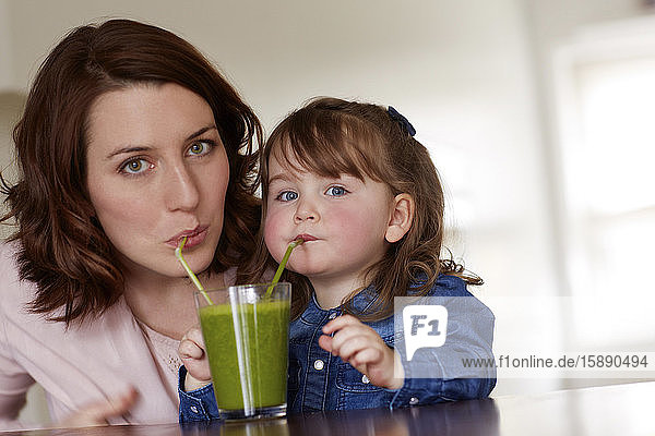 Portrait of young mother and little daughter drinking green smoothie together