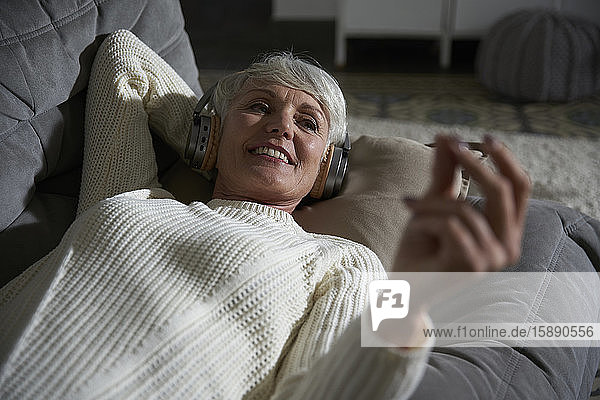 Porträt einer älteren Frau  die sich auf der Couch entspannt und mit Kopfhörern Musik hört