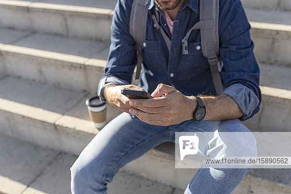 Schrägansicht eines auf einer Treppe sitzenden Mannes mit einem Smartphone