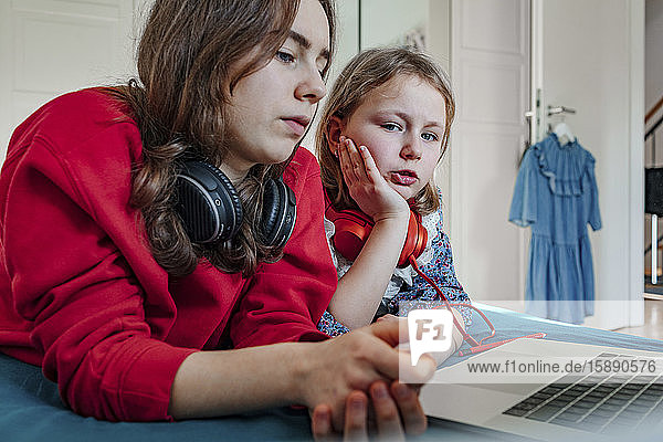Portrait of two sisters with headphones and laptop on bed