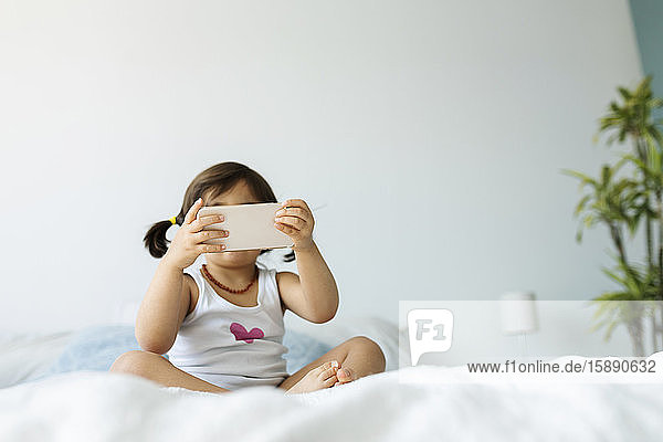 Little girl sitting on bed in underwear using smartphone