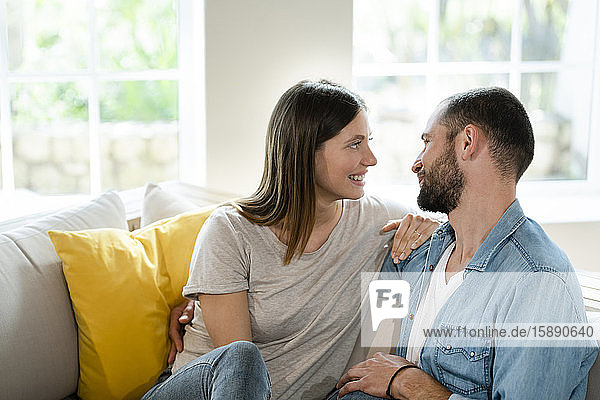 Zärtliches junges verliebtes Paar  das sich zu Hause auf der Couch anlächelt