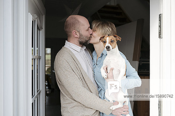 Happy couple with dog kissing at the entrance of their house