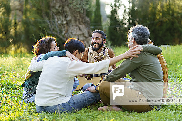Group of friends playing music and hugging on the grass in the field