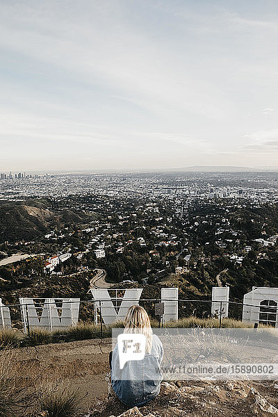Rückenansicht einer blonden Frau  die hinter einem Hollywood-Schild sitzt und auf die Aussicht schaut  Beverly Hills  USA