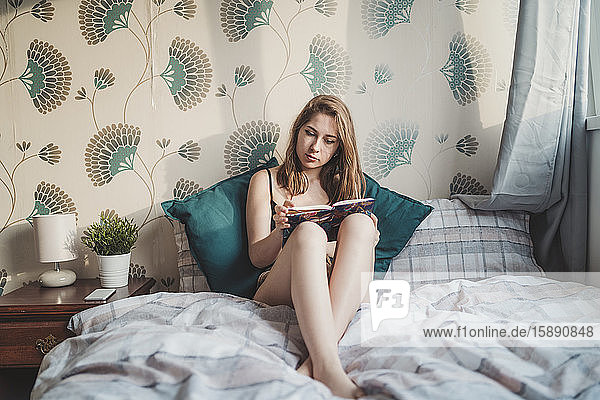Attraktive junge Frau sitzt zu Hause im Bett mit einem Buch