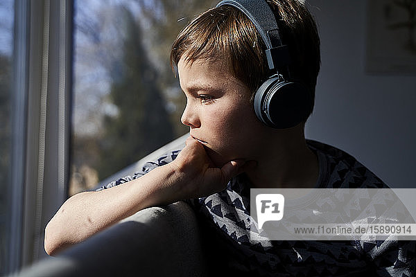 Profile of pensive boy listening music with headphones while looking out of window