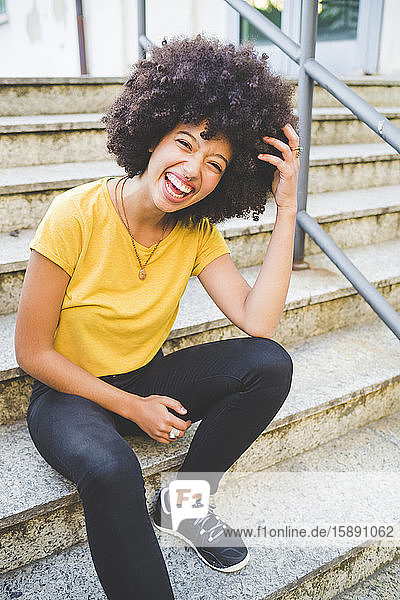 Porträt einer lachenden jungen Frau  die im Freien auf einer Treppe sitzt