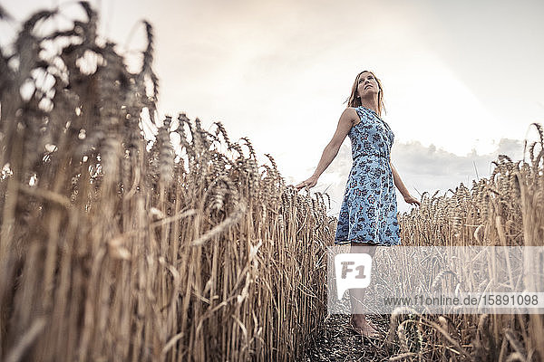 Barfüßige Frau steht in der Abenddämmerung in einem Weizenfeld