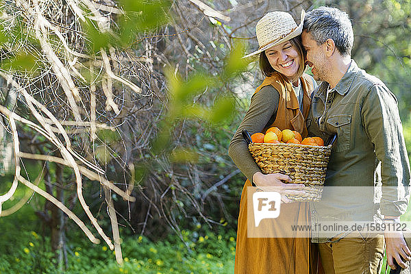 Heilsames Paar mit Korb voller Orangen auf dem Feld