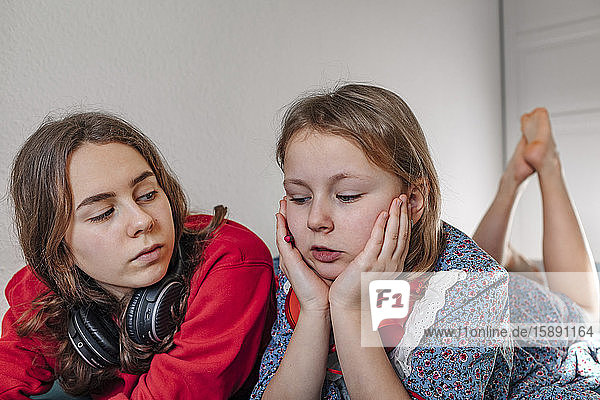 Portrait of two sisters with headphones lying together on bed