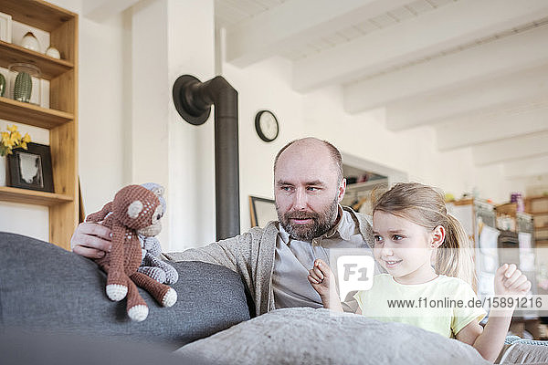 Vater und kleine Tochter sitzen zu Hause zusammen auf der Couch und spielen mit Spielzeug