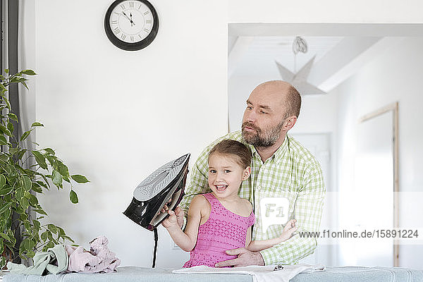 Father and happy daughter ironing together at home