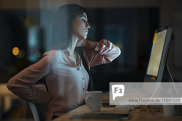 Young woman sitting at desk in office having back and neck pain
