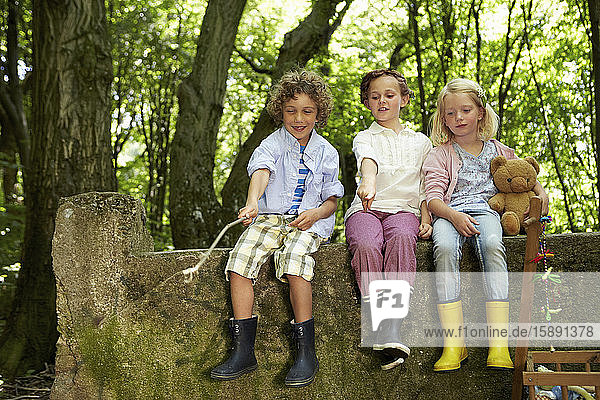 Children sitting on stone wall in forest