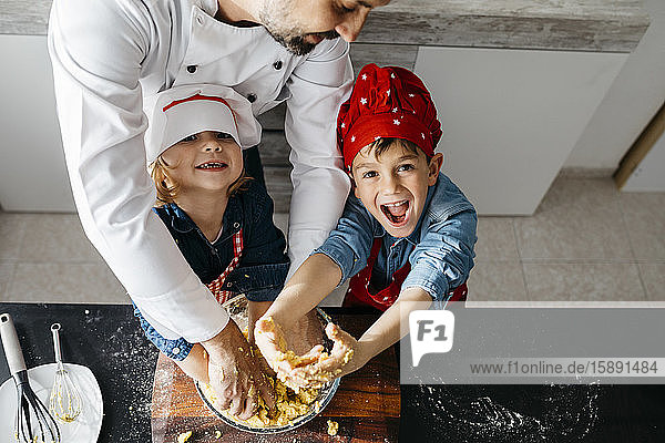 Portrait of happy kids preparing dough with father in kitchen at home