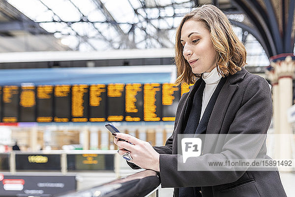 Woman at train station using mobile phone  London  UK