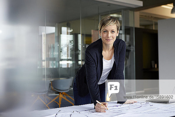 Porträt einer lächelnden Frau  die im Büro an einem Bauplan arbeitet