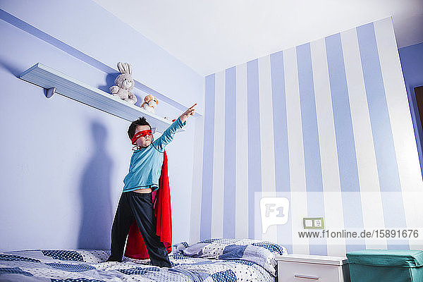 Kleiner Junge spielt Superheld und steht auf seinem Bett