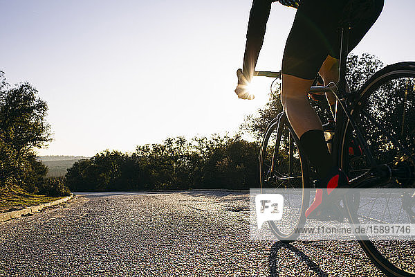 Nahaufnahme eines radfahrenden Athleten auf einer Landstraße bei Sonnenuntergang