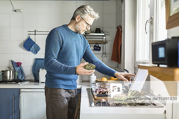 Mature man preparing salad in his kitchen using digital tablet