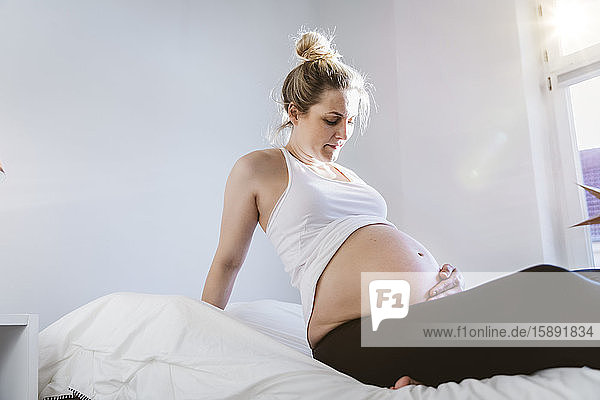 Schwangere Frau zu Hause im Bett sitzend