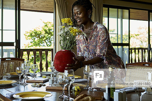 Lächelnde junge Frau stellt Blumenvase auf den Esstisch zu Hause