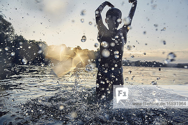 Silhouette eines Mädchens  das bei Sonnenuntergang in einem See planscht