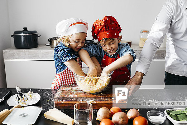Kinder bereiten mit dem Vater zu Hause in der Küche Teig zu
