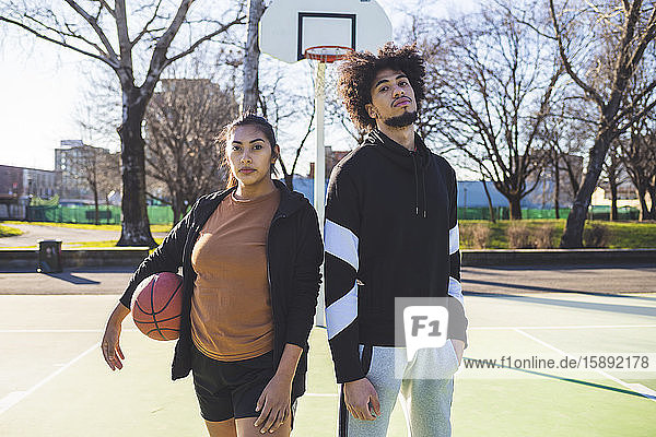 Porträt eines jungen Mannes und einer jungen Frau auf dem Basketballplatz stehend